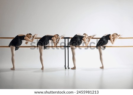 Tenderness in every move. Elegant beautiful teen girls, ballerinas training next to barre, showing flexibility against grey studio background. Ballet, art, dance studio, classical style, youth concept