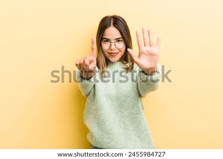 pretty hispanic woman smiling and looking friendly, showing number six or sixth with hand forward, counting down Royalty-Free Stock Photo #2455984727