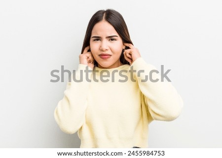 pretty hispanic woman looking angry, stressed and annoyed, covering both ears to a deafening noise, sound or loud music