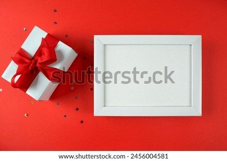 Top view photo of gift box and white wooden frame with empty space on red background. Place for text.