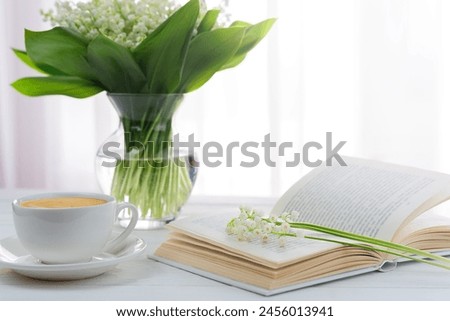 A bouquet of lilies of the valley, cup of morning cappuccino and book on the table. Weekend morning. Selective focus. Royalty-Free Stock Photo #2456013941