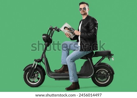 Cool young man with magazine on bike against green background