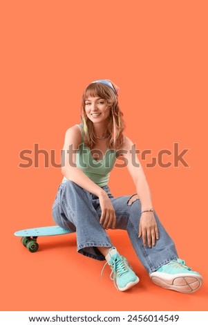 Young woman with skateboard sitting on orange background