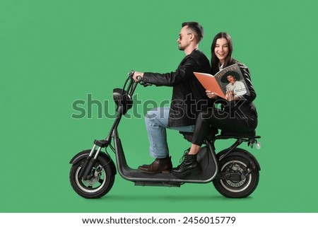 Cool young couple with magazine riding bike on green background