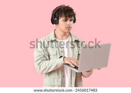 Male programmer in headphones working with laptop on pink background