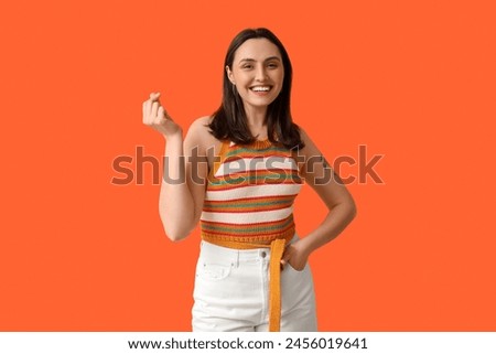 Smiling young woman showing heart gesture on orange background