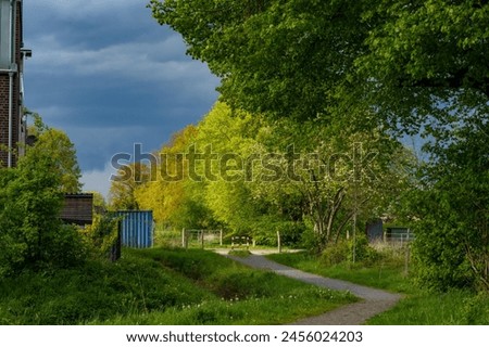 dark raincloud over green trees and a footpath in a residential area in Oldenburg (Germany) during spring Royalty-Free Stock Photo #2456024203