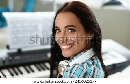 Close-up of smiling wonderful woman playing synthesizer on notes. Beautiful girl wearing fashionable smart earphones. Art music concept. Blurred background Royalty-Free Stock Photo #2456025277