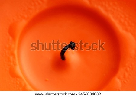 Close-up of a burning wick in orange candle wax