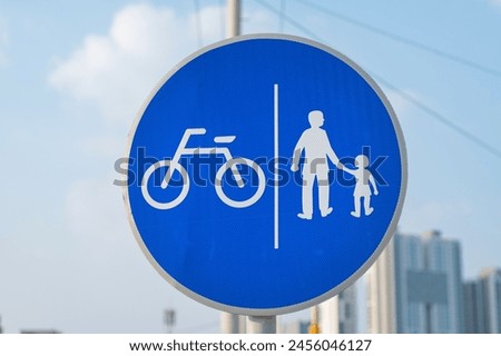 a road sign indicating a bike path and sidewalk. Silhouettes of people and a bicycle on a blue background with a white border.