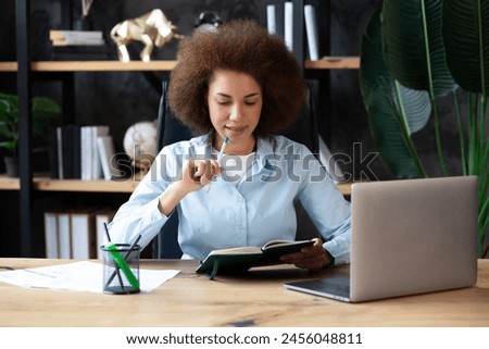 Pretty african american business woman working on laptop in office, businesswoman sitting at desk in office and thinking while working on laptop