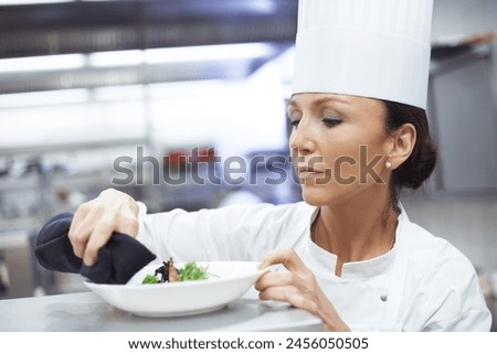 Professional, chef and woman or plating food, restaurant and executive cook and gourmet meal prep. Serious, catering and culinary presentation for fine dining, nutrition and hospitality industry Royalty-Free Stock Photo #2456050505