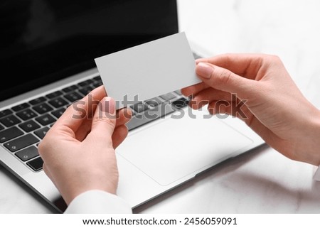 Woman with laptop holding blank business card at white table, closeup. Space for text