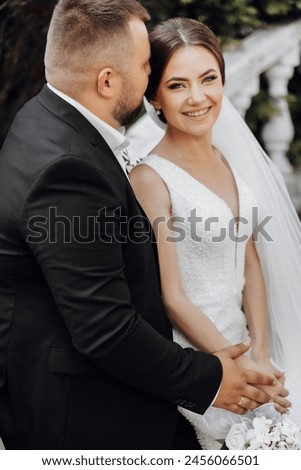 A bride and groom are posing for a picture. The bride is wearing a white dress and the groom is wearing a black suit. They are both smiling and looking at the camera