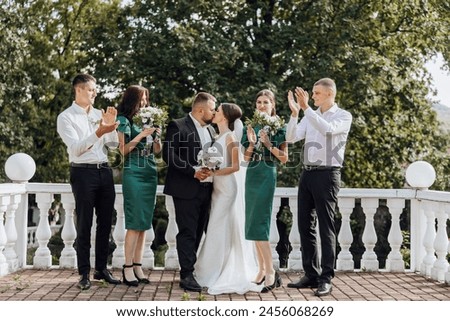 A group of people are posing for a picture, with a bride and groom in the center. The bride is wearing a green dress and the groom is wearing a suit