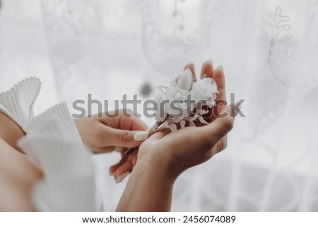 A woman is holding a flower in her hand. The flower is white and has a delicate appearance. The woman seems to be admiring the flower or preparing to use it for a special occasion