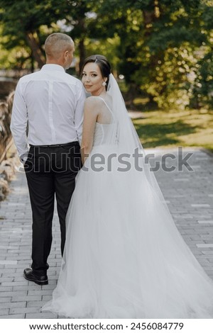 A bride and groom are posing for a picture on a brick walkway. The bride is wearing a white dress and the groom is wearing a white shirt. Scene is happy and celebratory