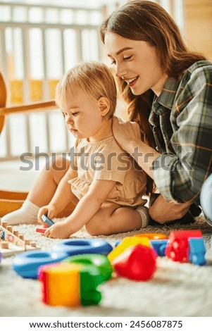A young mother happily engages with her toddler daughter on the floor, sharing love and laughter in a tender moment.