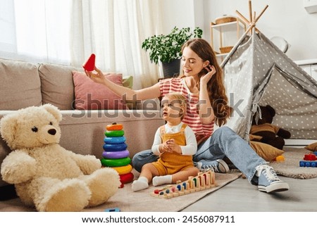 A young mother sits on the floor, cuddling her baby daughter and a teddy bear in a heartwarming display of love and connection.