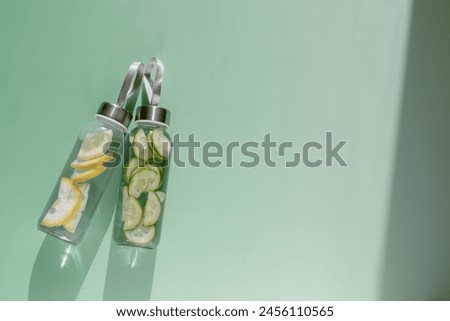 Glass bottles with lemon, cucumber water drink detox at sunlight on green colored fon, copy space. Healthy infused water boost metabolism, weight loss. Aesthetic still life, refreshing drink