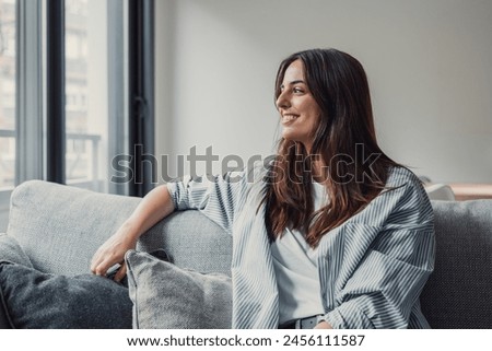 Portrait of happy dreamy young woman looking away, standing with folded arms in modern living room, visualizing future, recollecting good memories, planning weekend or thinking of problem solutions. Royalty-Free Stock Photo #2456111587