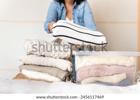 Woman stores or takes out winter sweaters from a box. Concept change of season in clothes closet