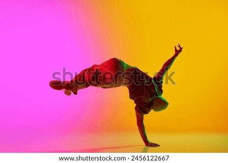 Dynamic photo of young, talented man dancing freestyle moves in neon light against gradient pink-yellow background. Concept of art, hobby, sport, creativity, fashion and style, action. Ad
