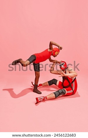 Boy in red suit with mask climbs with his fists towards man who sits in fear on floor against pink studio background. Plots for games. Concept of pop art, costume festivals, competitions. Ad
