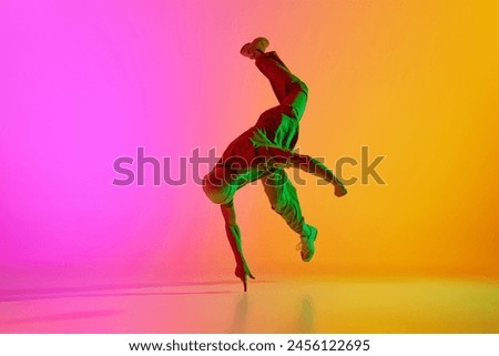 Dynamic photo of young, talented man dancing in freestyle in neon light against gradient pink-yellow background. Concept of art, hobby, sport, creativity, fashion and style, action. Ad