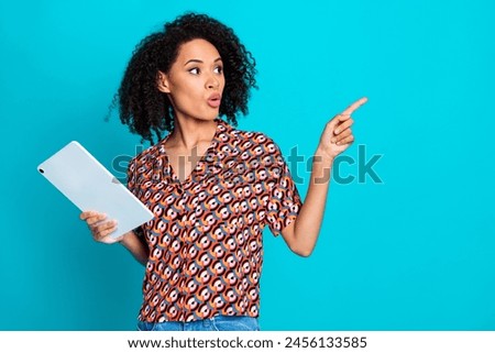 Portrait of impressed girl with wavy hair wear shirt hold tablet indicating look at sale empty space isolated on blue color background