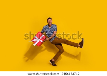 Full length photo of good mood guy wear print shirt buying christmas present walking empty space isolated yellow color background