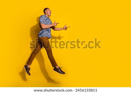 Full length photo of handsome good mood guy wear print shirt jumping high showing empty space isolated yellow color background