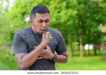 Photo of asian man suffers pain in throat and coughing due a virus or infection while sport at park. Stock photo
