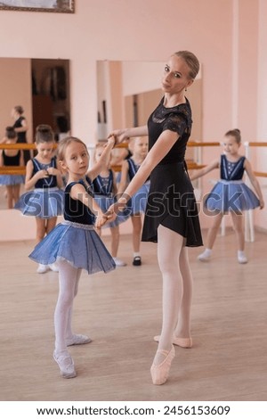 Children's ballet school. Caucasian woman teaching ballet to little girls. Vertical photo. 