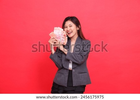 Cheerful Asian female director's expression with both hands holding credit, debit and money cards at the camera wearing a gray jacket and red skirt. for transaction, business and advertising concepts