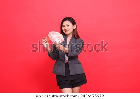 gesture of asian office woman smiling with both hands holding a credit card and money wearing a jacket and skirt on a red background. for financial, business and advertising concepts