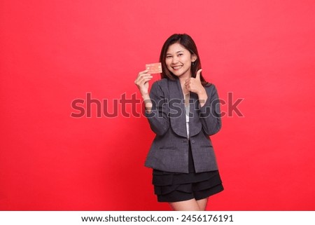 Asian businesswoman expression happy cool thumbs up sign and holding debit credit card wearing jacket and skirt red background. for financial, business and advertising concepts