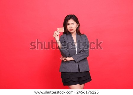 Asian businesswoman's expression is shocked, arms crossed and holding a debit credit card wearing a jacket and skirt on a red background. for financial, business and advertising concepts