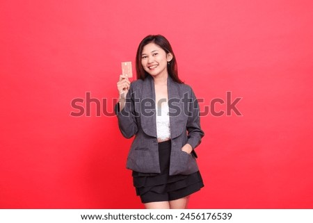 Cheerful indonesia office woman's expression holding a debit credit card in her pocket wearing a jacket and skirt on a red background. for financial, business and advertising concepts