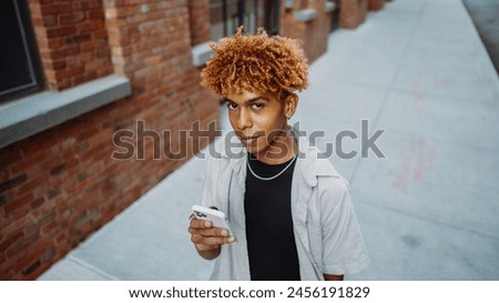 A young man is standing on a sidewalk looking at his cell phone