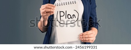 A woman holding a notepad with "plan" written on it, on a gray background, stock photo
