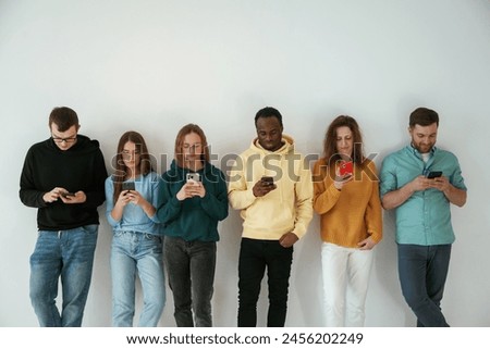 Busy by using smartphones. Group of young people are standing against white background.