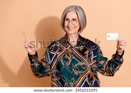 Photo of positive person wear print blouse in glasses hold debit card look directing empty space isolated on beige color background