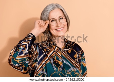 Photo of good mood clever cheerful person with gray hairstyle wear print blouse touch glasses smiling isolated on beige color background