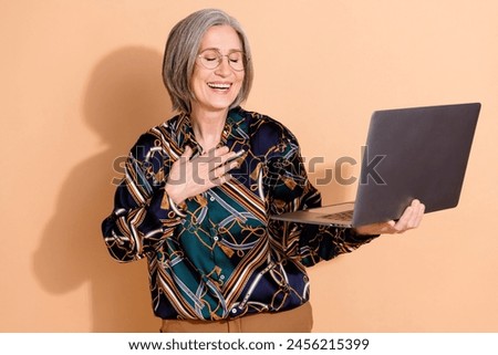 Photo of funny good mood person wear print blouse in glasses holding laptop palm on chest laughing isolated on beige color background