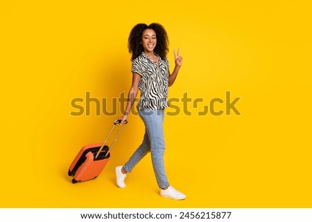 Portrait photo of glamour young charming woman curly hair in zebra print shirt with valise showing v sign isolated on yellow color background