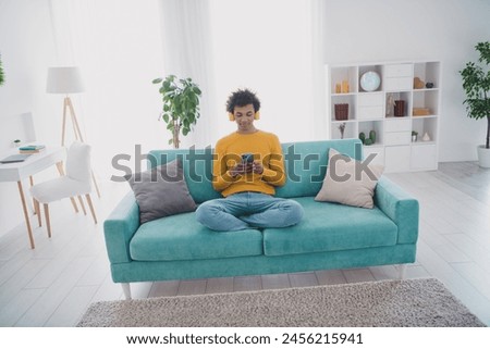 Full size photo of nice young man use smart phone wear yellow pullover white interior apartment indoors