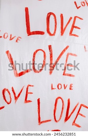 Multiple drawings of the word LOVE hand-painted in bright red forming a pattern on a plain white surface oilcloth, Valentine`s day concept celebration decoration in photo studio. Love, holiday, party