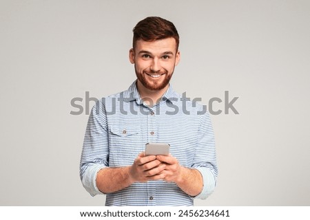 Young bearded man using his phone and smiling on studio background, panorama, copy space