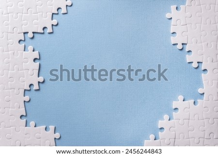 Frame of white puzzle elements on blue background. Business or educational concept. Selective focus, copy space Royalty-Free Stock Photo #2456244843